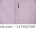 White metal grid fence against a textured pastel pink wall 127482384