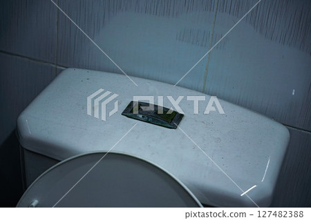 Dusty white toilet tank with a worn-out flush button in a restroom 127482388