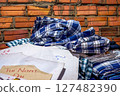 Blue and white plaid fabric piled on papers near a brick wall 127482390