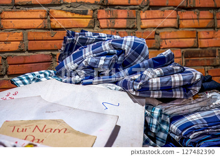 Blue and white plaid fabric piled on papers near a brick wall Blue and white plaid fabric piled on papers near a brick wall 127482390