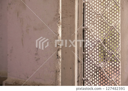 Close up of a weathered white wall next to a perforated metal sheet Close up of a weathered white wall next to a perforated metal sheet 127482391