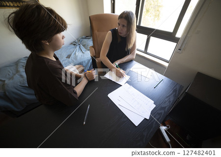 Private tutor helping young student with homework at home Private tutor helping young student with homework at home 127482401