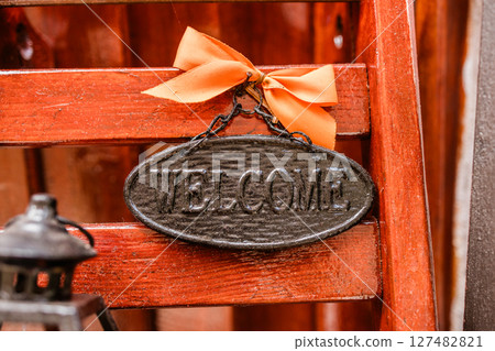 Rustic welcome sign with orange ribbon on wooden background. Home decor, hospitality greeting, and cozy entrance details. Rustic welcome sign with orange ribbon on wooden background. Home decor, hospitality greeting, and cozy entrance details. 127482821