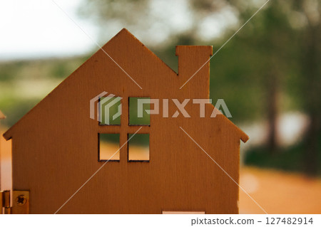 Wooden toy house against natural eco green blurred background. A home in a forest, woods. Cardboard house with window, roof. Ecological rural building Wooden toy house against natural eco green blurred background. A home in a forest, woods. Cardboard house with window, roof. Ecological rural building 127482914