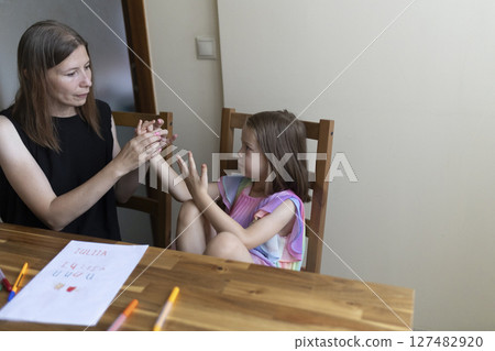 Teacher helping young girl learning sign language at home 127482920