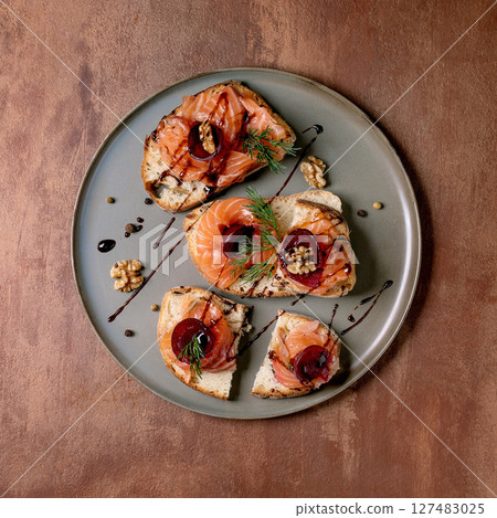 Sandwiches with thinly sliced salted salmon fillet, beetroot slices, walnuts, balsamic vinegar and fresh wheat bread on grey plate, fine dining. Brown background, top view. Colors of the year 2025. Sandwiches with thinly sliced salted salmon fillet, beetroot slices, walnuts, balsamic vinegar and fresh wheat bread on grey plate, fine dining. Brown background, top view. Colors of the year 2025. 127483025