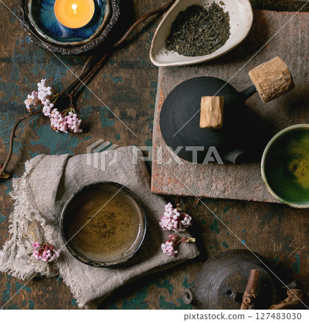 Chinese Tea Ceremony. Two traditional handmade ceramic black teapot with wooden handle on dark wooden table. Ceramic teacups and pink spring flowers, burning tea candle. Tea ceramics. Top view, space Chinese Tea Ceremony. Two traditional handmade ceramic black teapot with wooden handle on dark wooden table. Ceramic teacups and pink spring flowers, burning tea candle. Tea ceramics. Top view, space 127483030