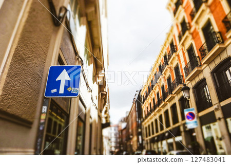 A rectangular sign with a white arrow on a city street indicates forward movement. European architecture in sunny day. Empty morning street in daytime A rectangular sign with a white arrow on a city street indicates forward movement. European architecture in sunny day. Empty morning street in daytime 127483041
