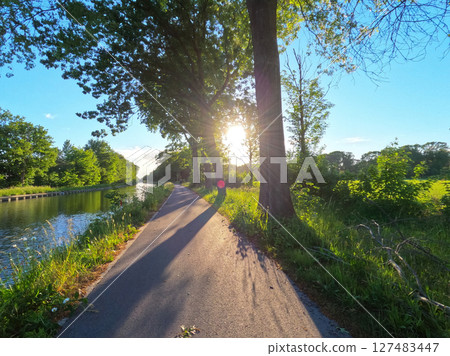 The Scenic Pathway Runs Along a Beautiful Canal, Bathed in Sunlight and Surrounded by Lush Greenery The Scenic Pathway Runs Along a Beautiful Canal, Bathed in Sunlight and Surrounded by Lush Greenery 127483447