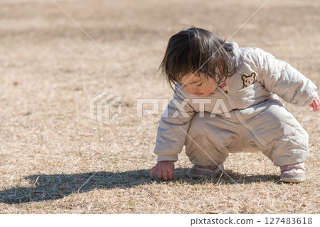 [One-year-old child crouching down while playing on the grass at Sagamihara Municipal Asamizo Park] 127483618