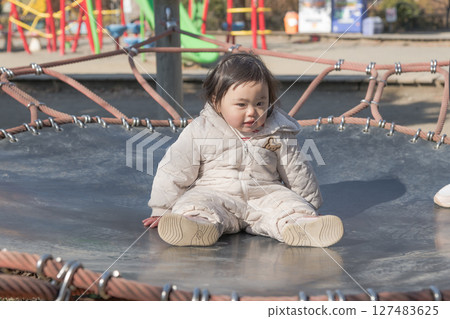 [A one-year-old child playing on a trampoline in the children's playground at Sagamihara City Asamizo Park] 127483625