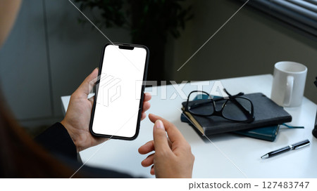 Close up of woman holding smartphone with blank screen in modern office Close up of woman holding smartphone with blank screen in modern office 127483747