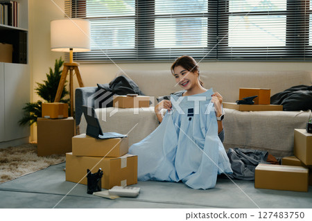 Smiling woman showing new clothes during an online live stream at home Smiling woman showing new clothes during an online live stream at home 127483750