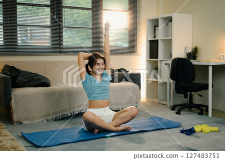 Young woman stretching arms on a yoga mat at home during morning workout 127483751