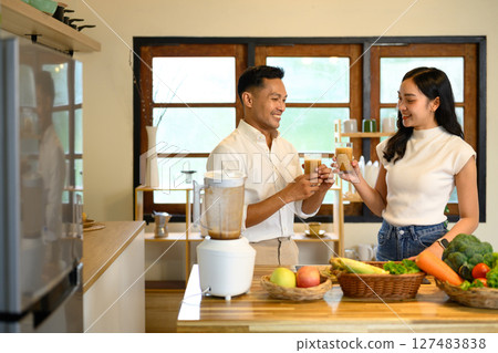 Happy couple enjoying fresh homemade smoothies together in the kitchen Happy couple enjoying fresh homemade smoothies together in the kitchen 127483838