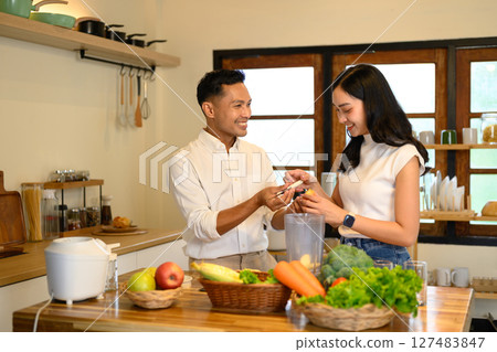 Happy couple preparing fresh fruit smoothies together in a cozy kitchen 127483847