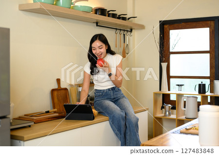 Happy woman enjoys a healthy snack and using digital tablet in the kitchen 127483848