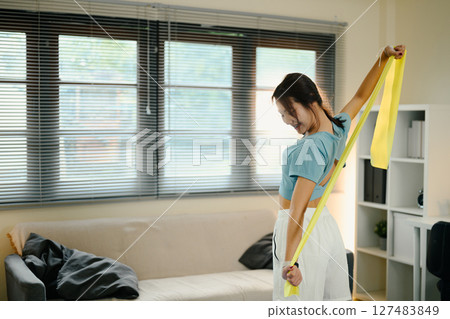Active female stretching with a yellow resistance band during a home workout session Active female stretching with a yellow resistance band during a home workout session 127483849