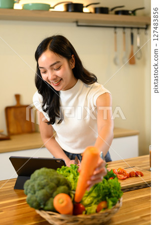Smiling woman preparing healthy food and following a recipe on digital tablet in a kitchen 127483856