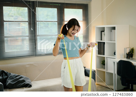 Active female stretching with a yellow resistance band during a home workout session 127483860