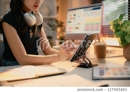 Female graphic designer using a digital tablet at a modern desk with color swatches Female graphic designer using a digital tablet at a modern desk with color swatches 127483863