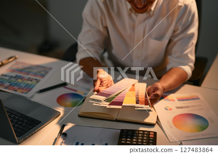 Graphic designer selecting color swatches from a palette book at a creative desk Graphic designer selecting color swatches from a palette book at a creative desk 127483864