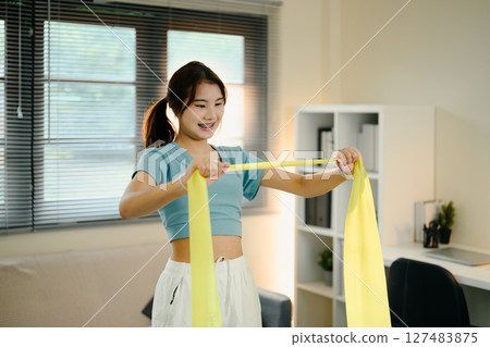 Active female stretching with a yellow resistance band during a home workout session 127483875