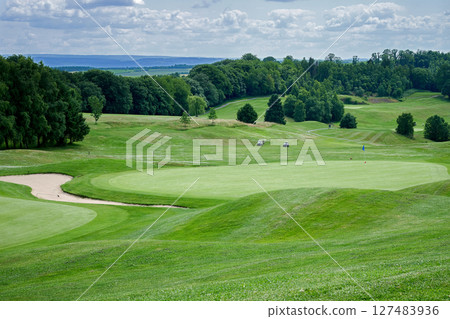 Smooth grassy area of a golf course, trees in the background 127483936