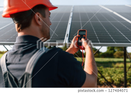 Measuring the electricity by using device. Man is doing operating and maintenance in solar power plant Measuring the electricity by using device. Man is doing operating and maintenance in solar power plant 127484071