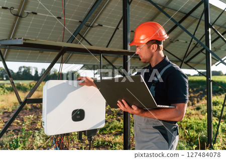 Standing and holding laptop. Man is doing operating and maintenance in solar power plant 127484078