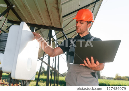 Standing and holding laptop. Man is doing operating and maintenance in solar power plant 127484079