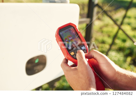 Holds a thermal imager. Close up view of man that is doing operating and maintenance in solar power plant 127484082