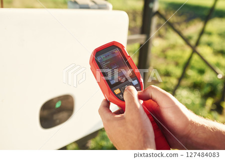Holds a thermal imager. Close up view of man that is doing operating and maintenance in solar power plant Holds a thermal imager. Close up view of man that is doing operating and maintenance in solar power plant 127484083