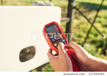 Holds a thermal imager. Close up view of man that is doing operating and maintenance in solar power plant 127484084