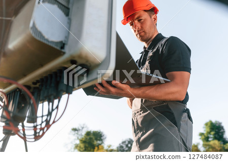 Standing and holding laptop. Man is doing operating and maintenance in solar power plant Standing and holding laptop. Man is doing operating and maintenance in solar power plant 127484087