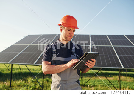 Summer time, standing and holding digital tablet. Man is doing operating and maintenance in solar power plant 127484112