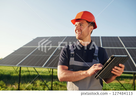 Summer time, standing and holding digital tablet. Man is doing operating and maintenance in solar power plant 127484113