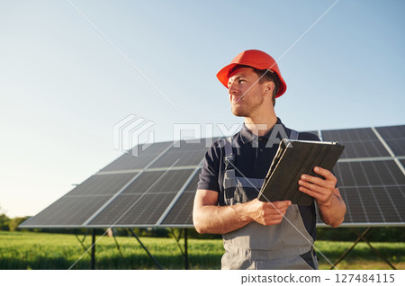 Summer time, standing and holding digital tablet. Man is doing operating and maintenance in solar power plant 127484115