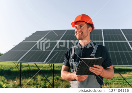 Summer time, standing and holding digital tablet. Man is doing operating and maintenance in solar power plant 127484116