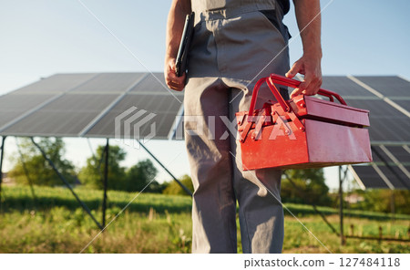 Walking and holding repair toolbox. Close up view of man that is doing maintenance in solar power plant Walking and holding repair toolbox. Close up view of man that is doing maintenance in solar power plant 127484118