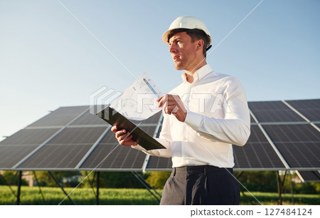 Notepad with document is in hands. Man is doing operating and maintenance in solar power plant Notepad with document is in hands. Man is doing operating and maintenance in solar power plant 127484124
