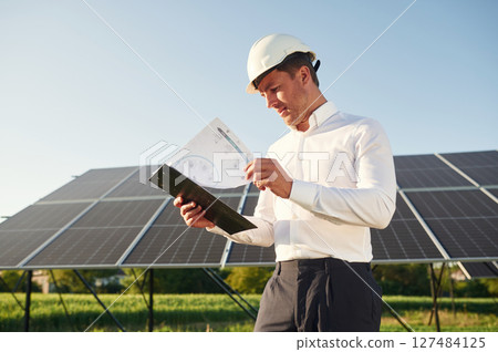 Notepad with document is in hands. Man is doing operating and maintenance in solar power plant 127484125