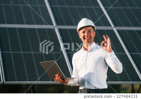 Modern laptop is in hands. Man is doing operating and maintenance in solar power plant 127484131
