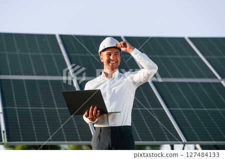 Front view, holding laptop. Man is doing operating and maintenance in solar power plant 127484133