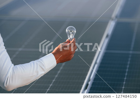 Close up view of man's hand that is holding light bult in front of solar panel Close up view of man's hand that is holding light bult in front of solar panel 127484150