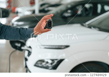 Hand is holding the keys. Close up view of man that is with electrical car 127484429