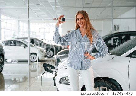 Keys in hands. Beautiful woman is indoors with the modern car 127484476