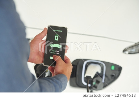 Charging process on the smartphone app. Close up view of man that is with electrical car Charging process on the smartphone app. Close up view of man that is with electrical car 127484518