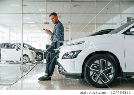 Handsome car dealership worker is with electric vehicle Handsome car dealership worker is with electric vehicle 127484521