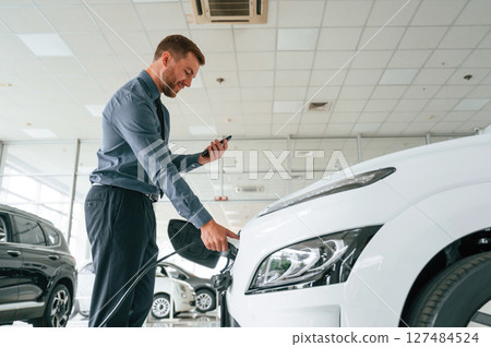 Plugging the charger. Handsome car dealership worker is with electric vehicle Plugging the charger. Handsome car dealership worker is with electric vehicle 127484524